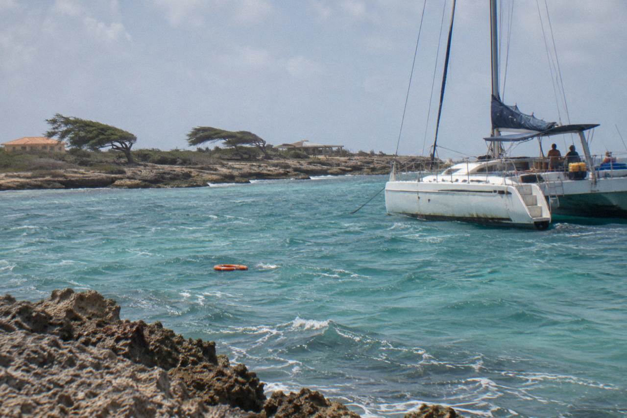 A large sailing catamaran moored over pale turquoise water near a Caribbean reef