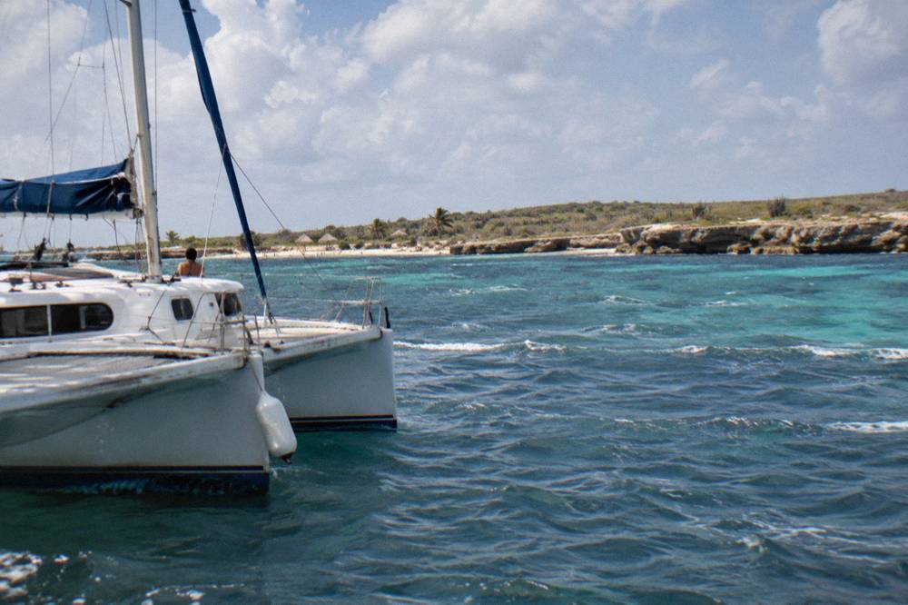 A catamaran anchored near a reef in calm turquoise water under scattered clouds