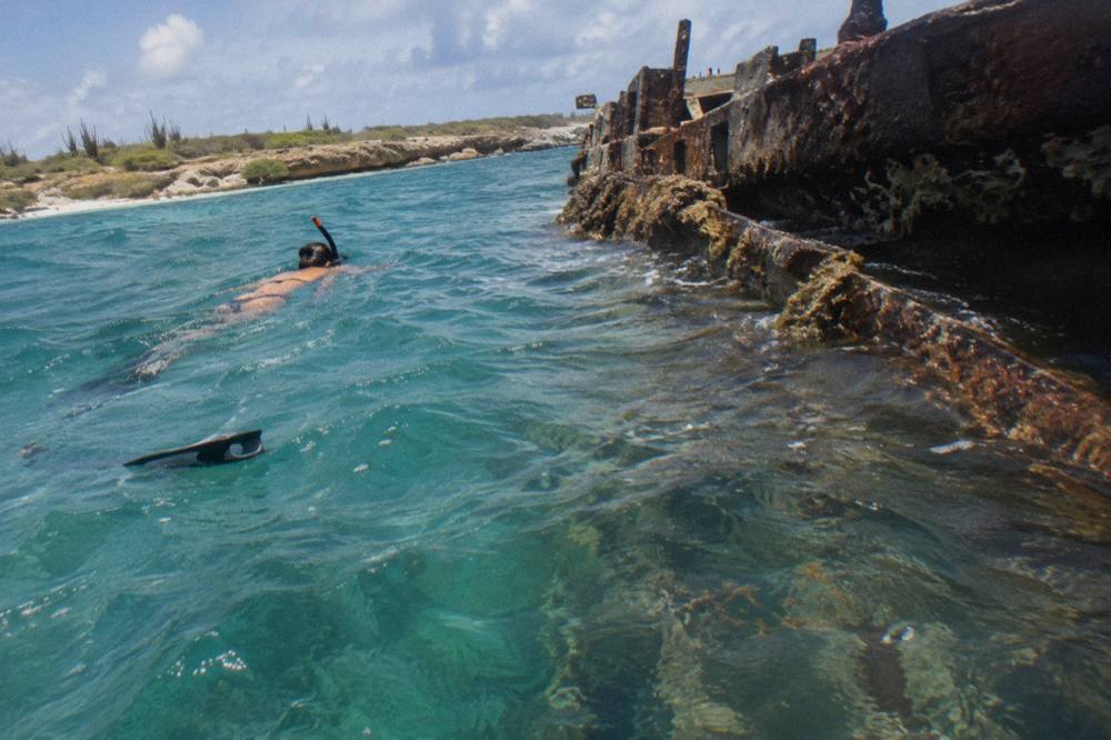 A snorkeler floating above the tilted hull of a sunken ship in clear turquoise water