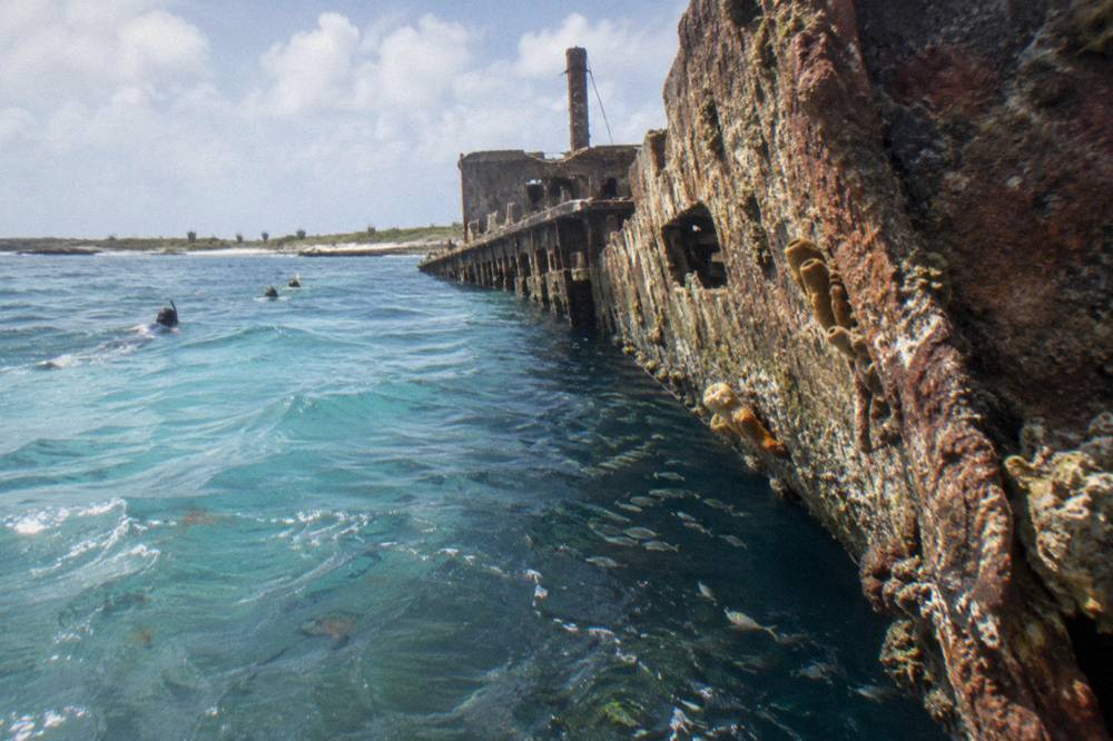 The coral encrusted hull of a sunken cargo ship sloping down toward darker deep water