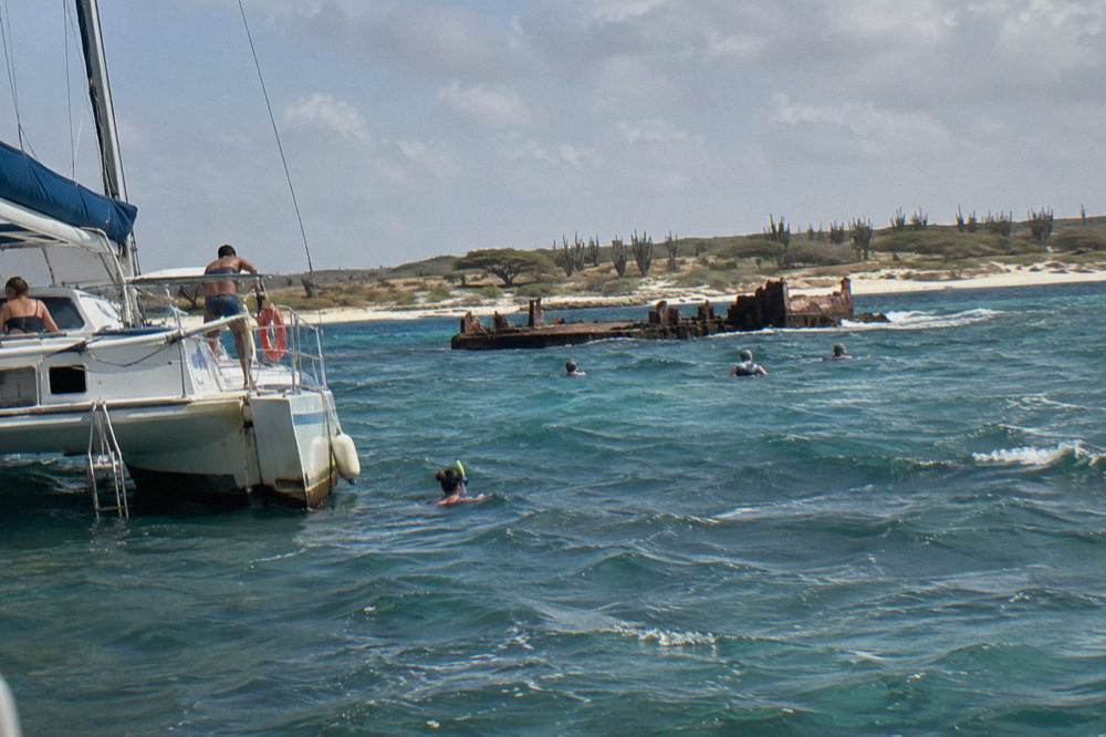 A catamaran anchored above a shallow shipwreck site with guests in the water snorkeling