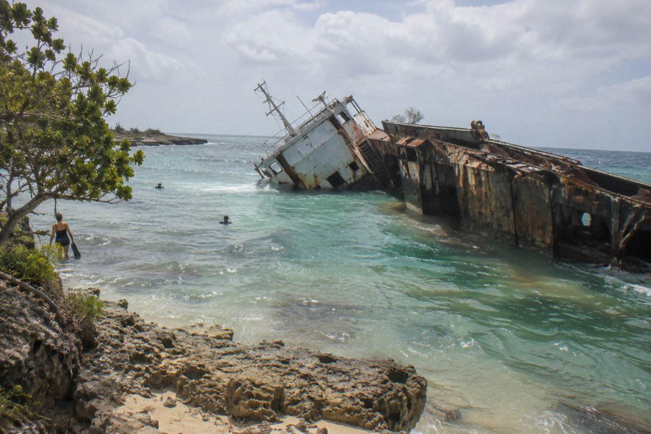 A sunken shipwreck resting on its side beneath pale green seawater near the surface