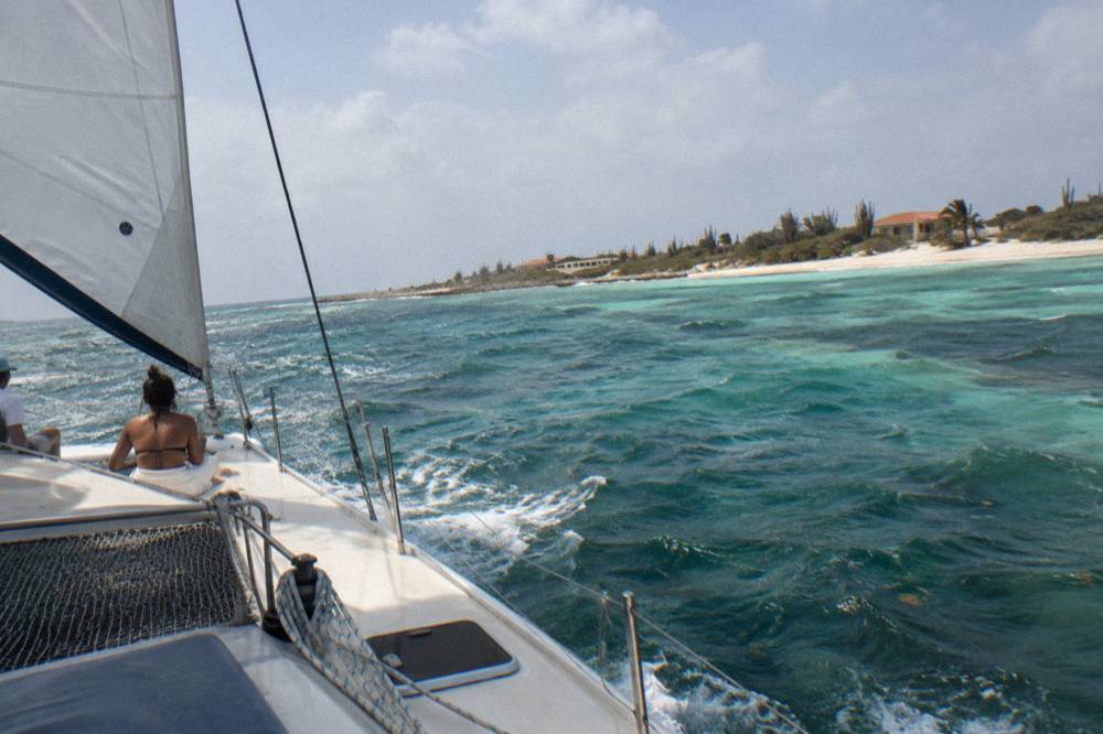 A catamaran under sail along a calm coastline with reef water below