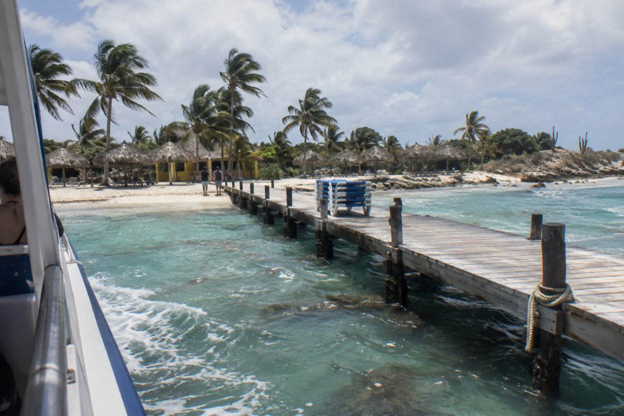 A small offshore island with a wooden ferry dock and clear shallow water over pale sand