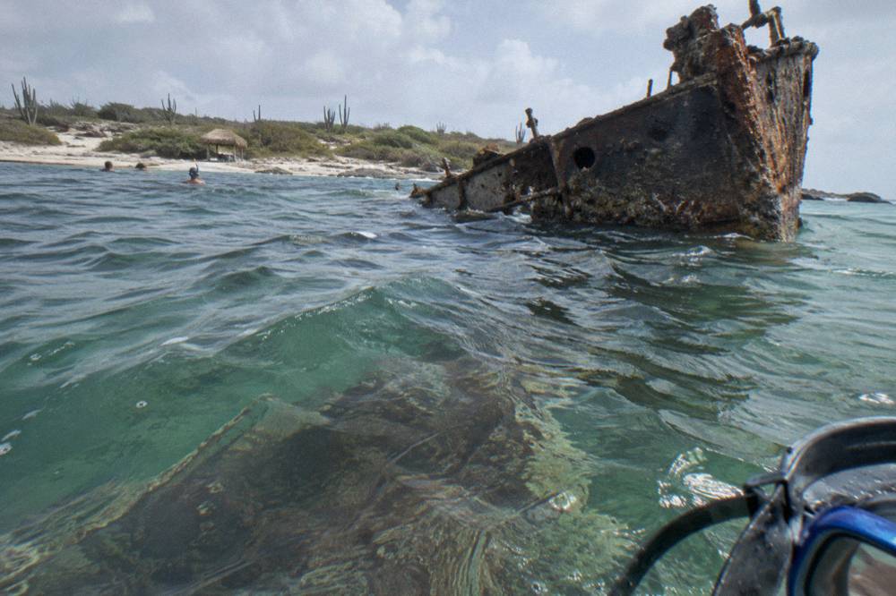 A shipwreck structure visible beneath clear blue water from the surface