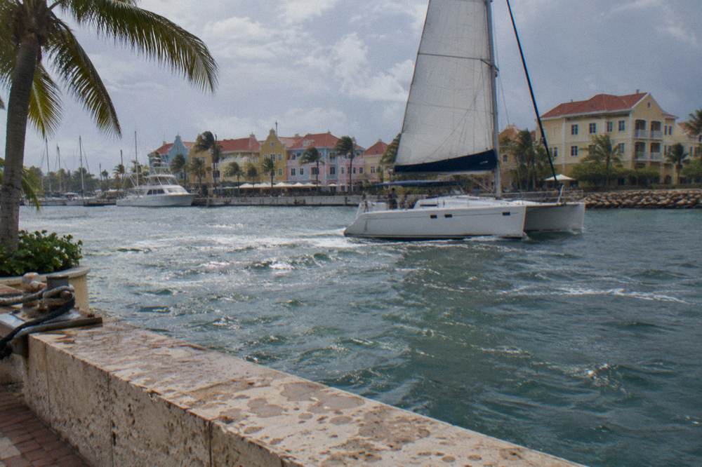 Catamaran under sail along a calm Caribbean coastline in late afternoon light