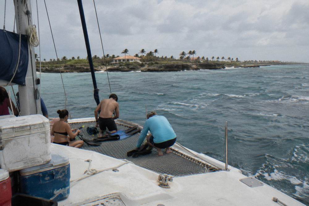 A catamaran anchored near a reef with guests preparing snorkel gear on deck