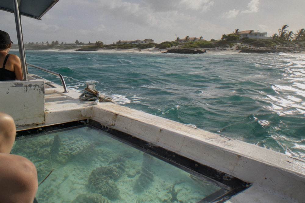 A small boat with a clear hull panel drifting over pale sand and coral