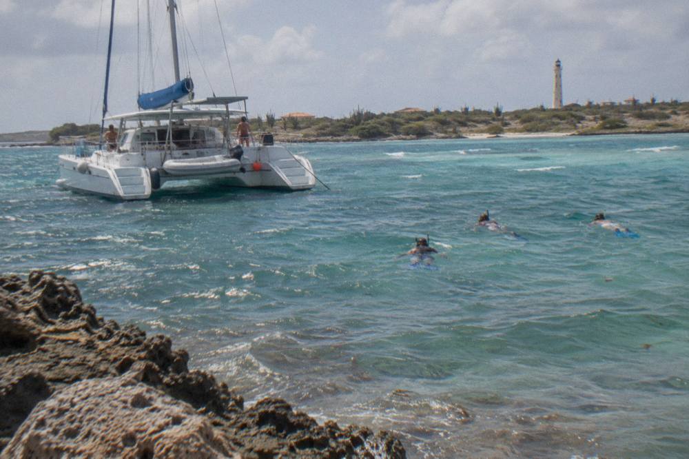 A catamaran anchored over pale blue shallows with snorkelers in the water nearby