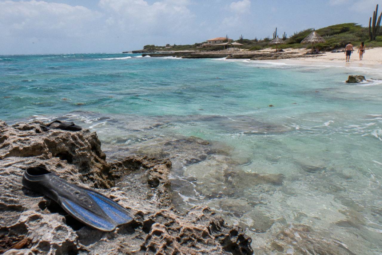 Calm turquoise water over a shallow reef close to a sandy shoreline under a bright sky
