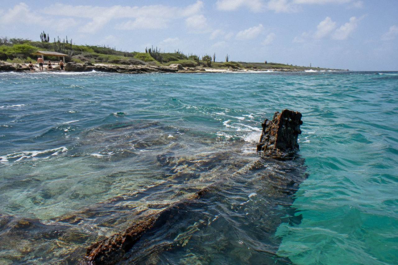 The bow section of a large sunken ship resting below calm turquoise water near a coral reef