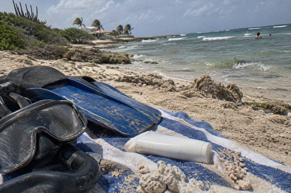 A tube of mineral sunscreen resting on a towel beside snorkel mask and fins
