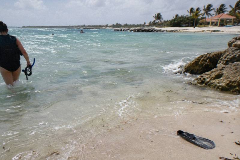 Snorkeler entering the water from a small sandy beach on the south coast of Aruba