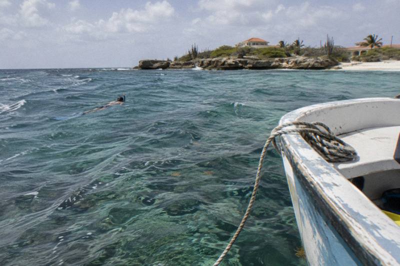 Small private boat moored over a reef off Aruba with a snorkeler swimming nearby