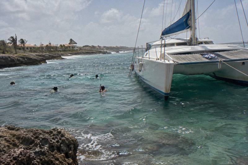 Sailing catamaran anchored over a shallow reef off Aruba with snorkelers in the water