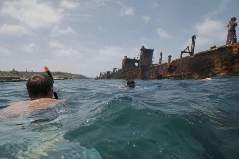 Snorkelers floating above a sunken shipwreck in clear water off Aruba