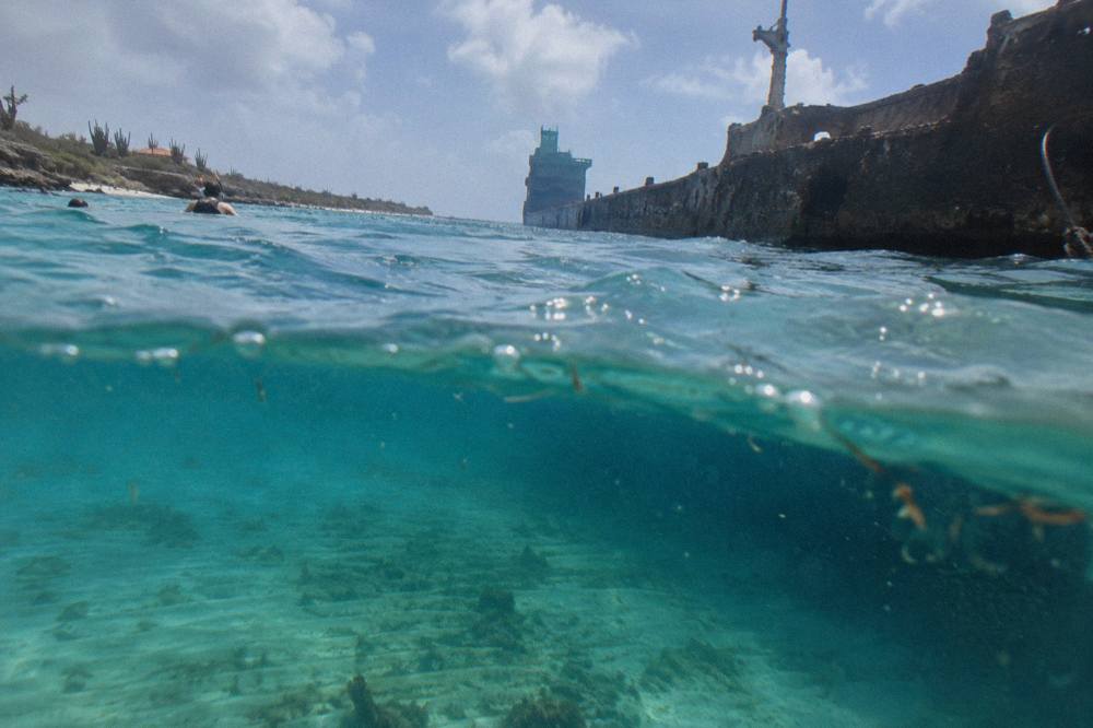The long hull of a sunken cargo ship visible beneath clear turquoise water