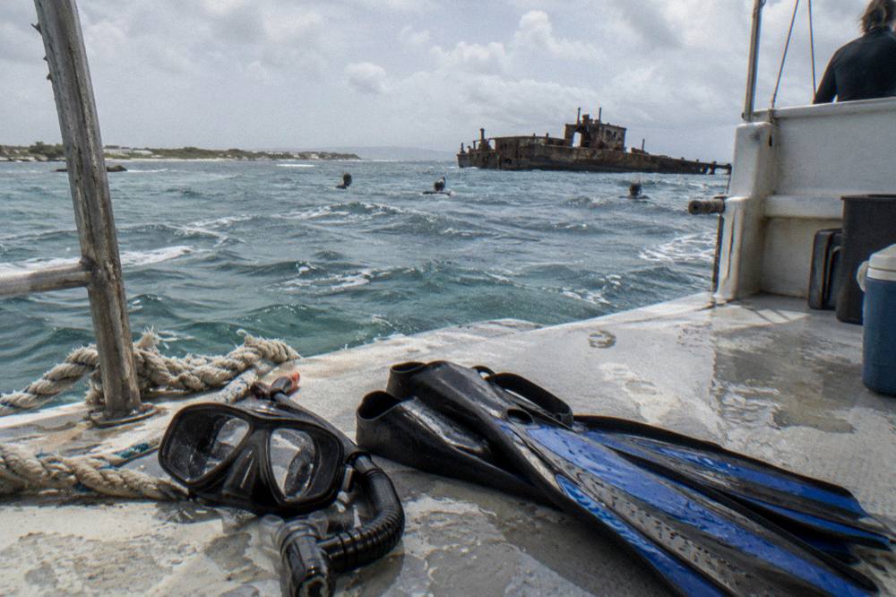 Snorkel fins and a mask resting on a boat deck beside calm sea water
