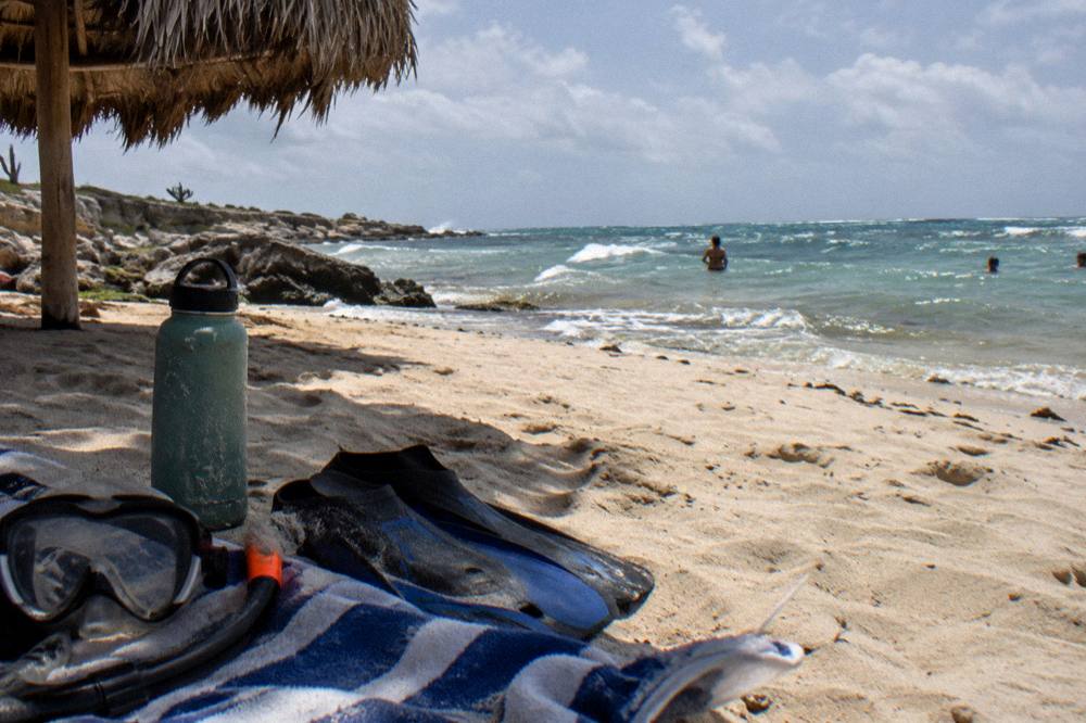 A mask, snorkel and fins resting on a towel beside a water bottle on sand