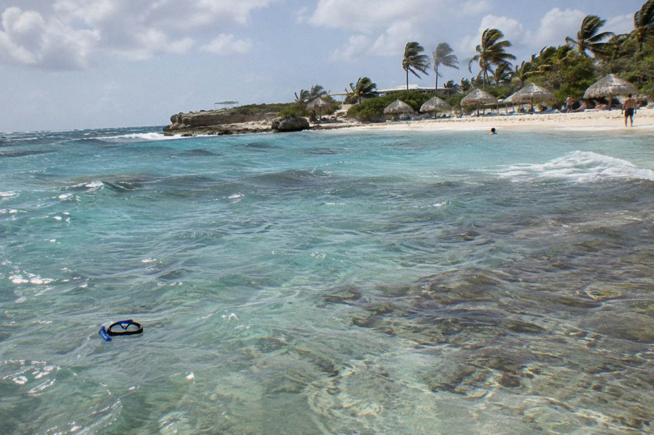 Calm turquoise water over a shallow reef with scattered coral heads near a sandy beach