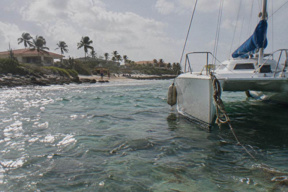 A sailing catamaran moored over clear shallow water near a reef