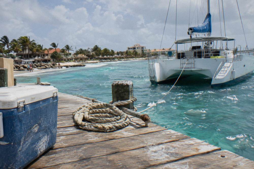 A wooden pier extending into calm blue water with a moored sailing catamaran