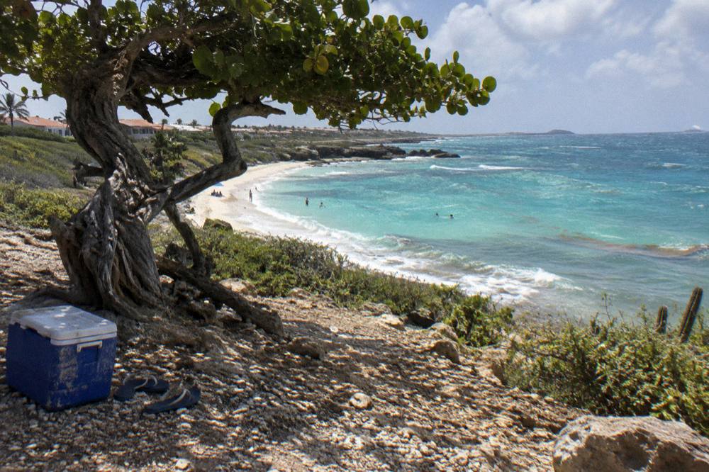 A sunny coastline with calm water and white sand under scattered clouds