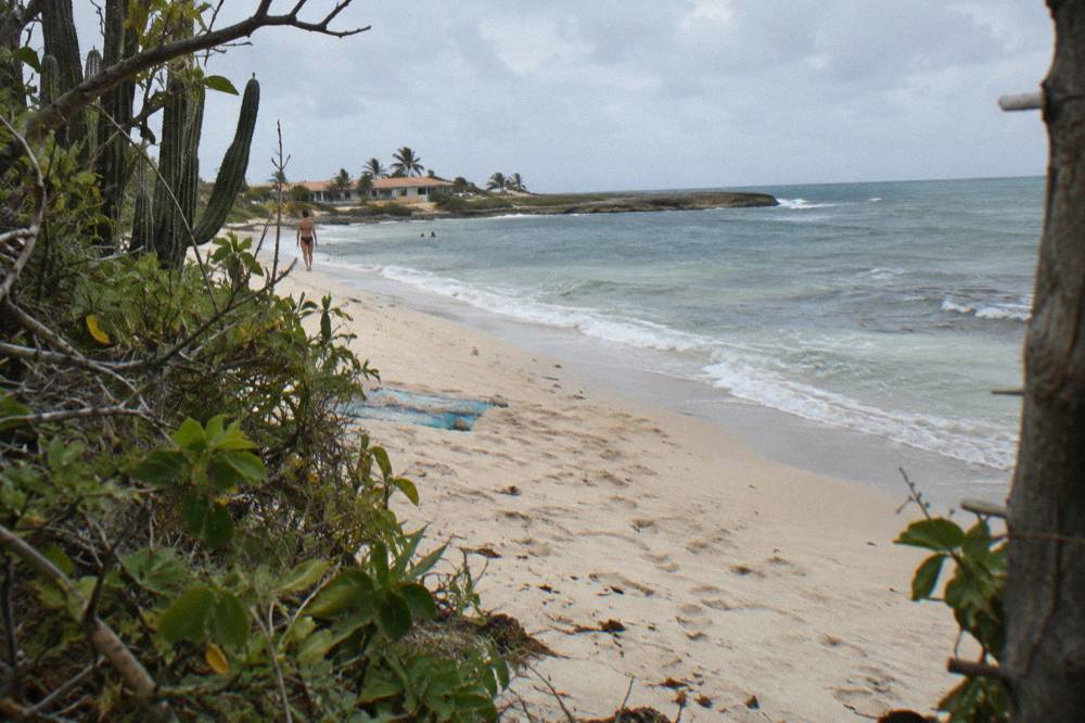 Sandy shoreline with calm shallow water and a rocky point along the coast