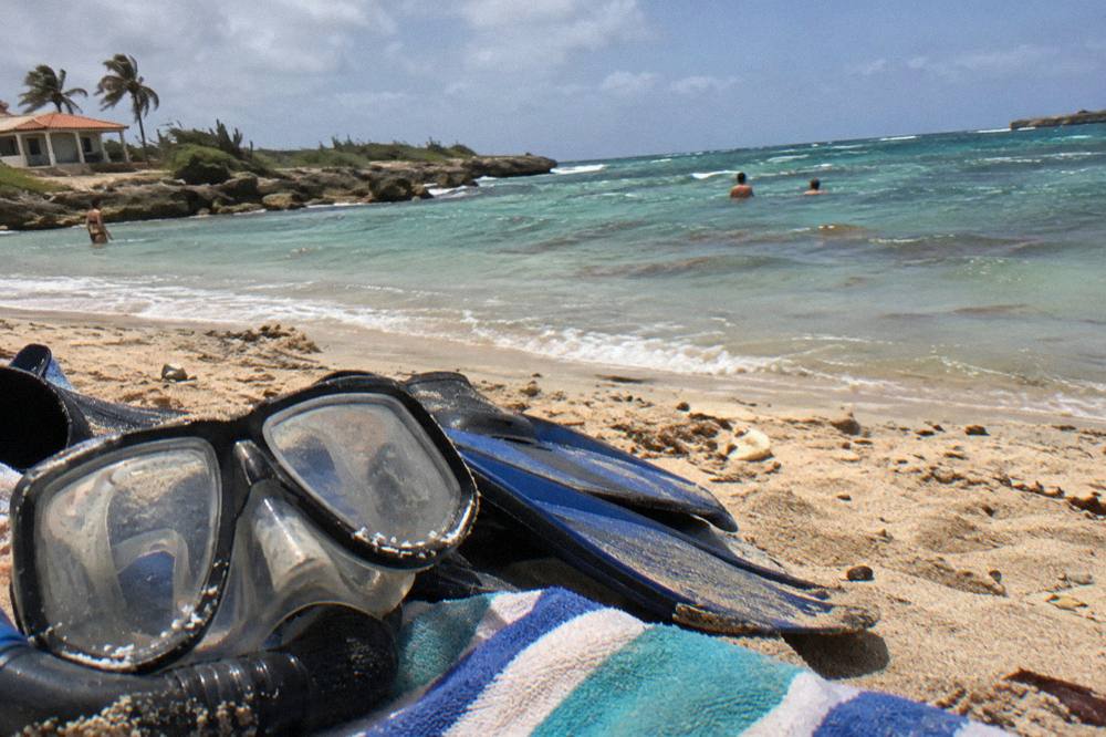 Snorkel mask and fins resting on a towel beside calm shallow water