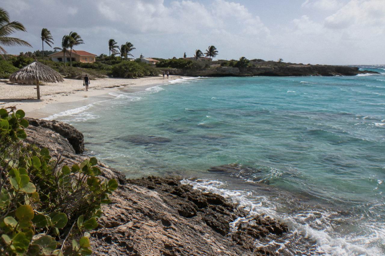 Calm turquoise bay with a shallow reef close to a sandy shoreline under a clear sky