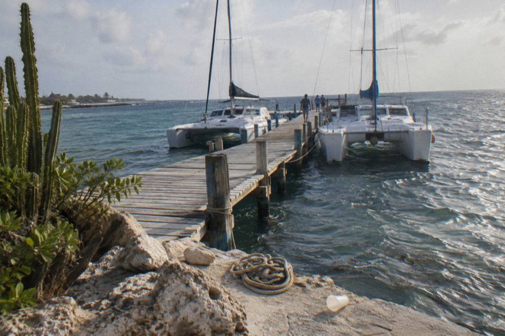 A wooden pier extending into calm blue water with catamarans moored alongside