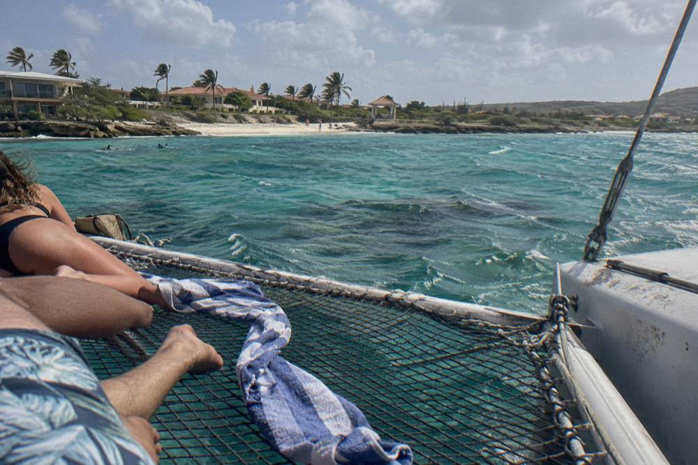 Passengers relaxing on the netting between a catamaran hulls above shallow reef water