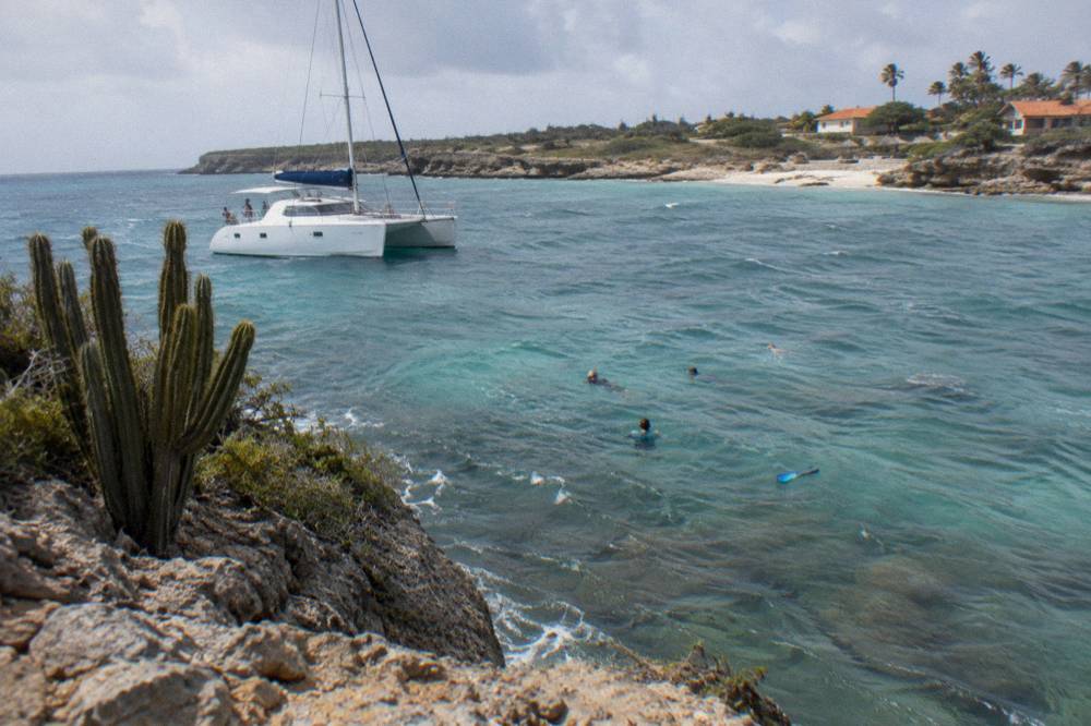 A catamaran moored over turquoise water with snorkelers near a reef below