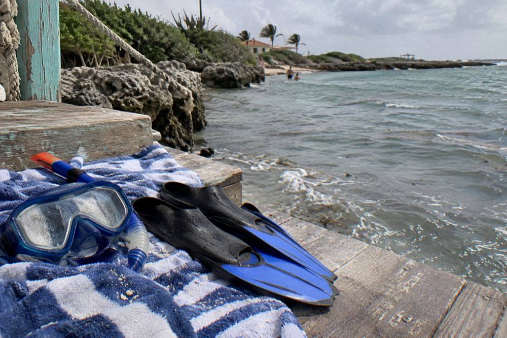 Snorkel mask and fins resting on a towel beside calm bay water