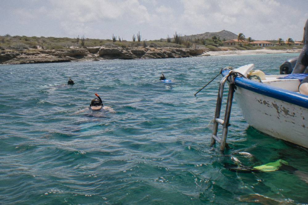 An open-air bus parked beside a calm turquoise lagoon with a sandy shore