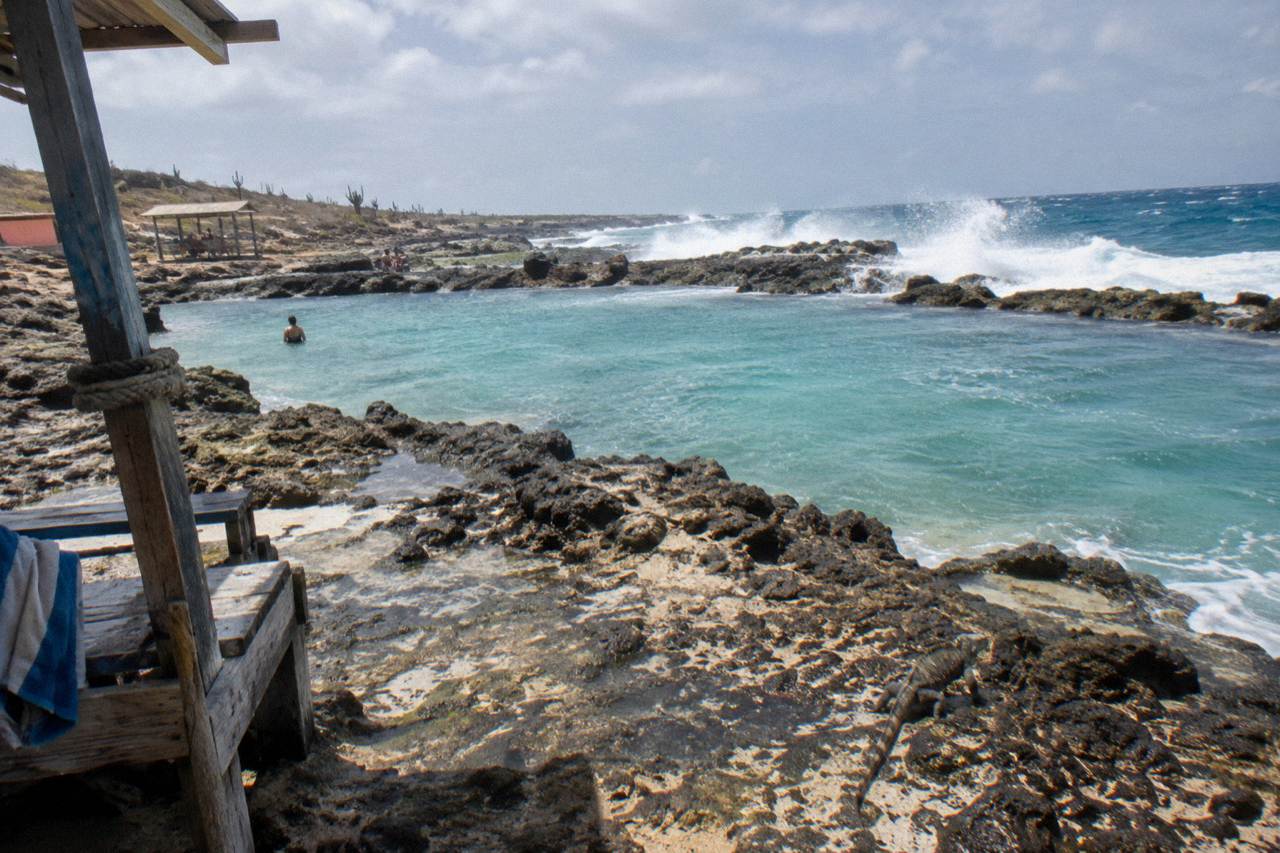A natural rock pool ringed by dark volcanic stone with clear turquoise water on a rocky shoreline