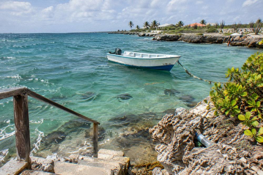 A calm bay with a moored boat and underwater rocks visible through clear green water