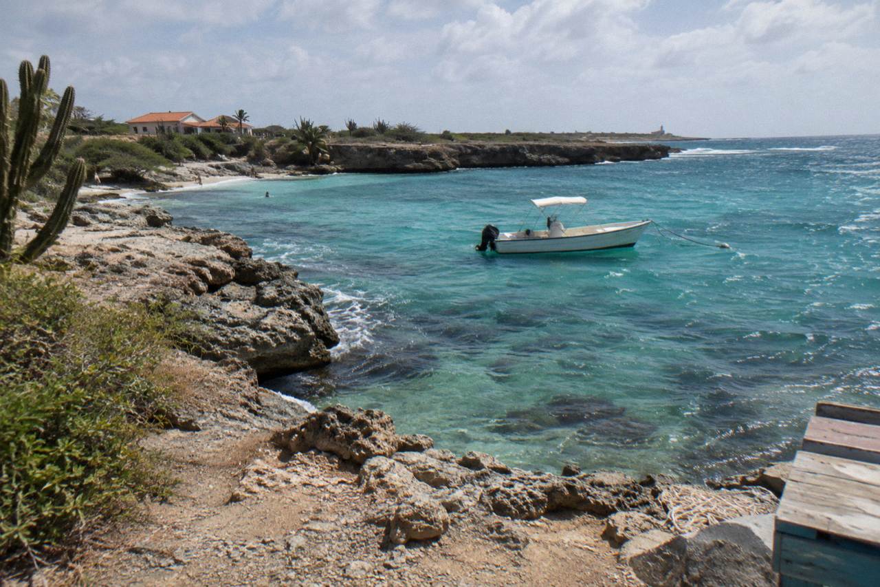 A small private boat anchored over a calm turquoise bay with a rocky reef below the surface