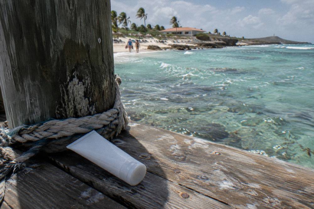 Close up of a mineral sunscreen tube on a wooden dock with clear shallow water behind