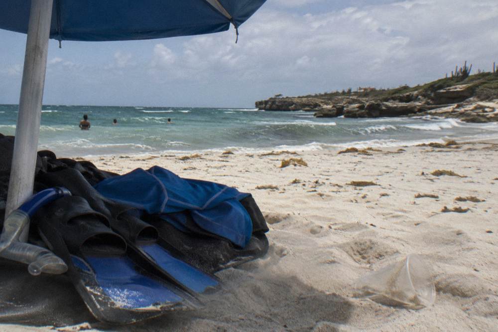Beach umbrella and snorkel fins on white sand under a bright midday sky