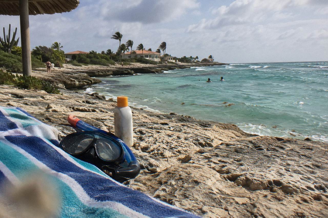 Sunscreen bottle and snorkel mask resting on a beach towel beside calm turquoise water