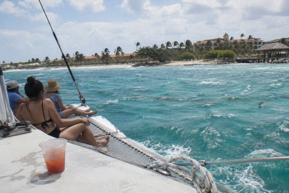 A catamaran under sail on open water with passengers seated along the netting