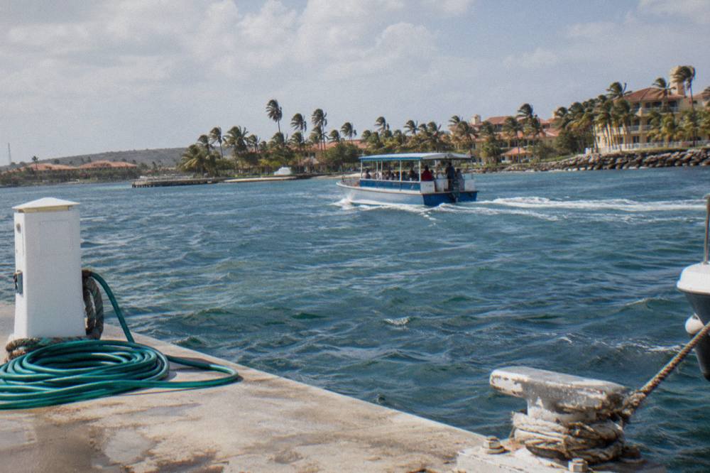 A ferry crossing calm harbor water toward a small island with palm trees