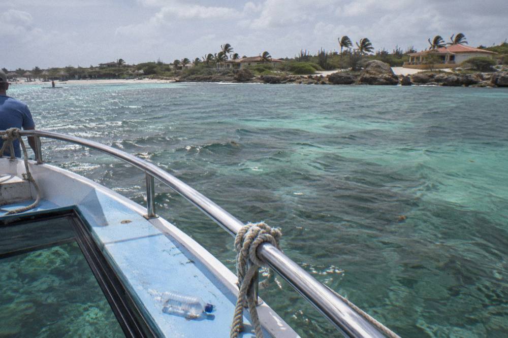 A small glass bottom boat drifting over pale sand and reef in clear shallow water