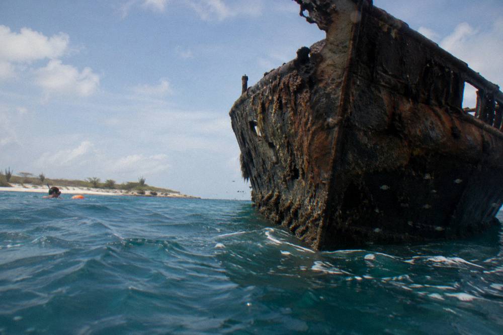 The dark hull of a sunken ship resting in clear blue water near the surface
