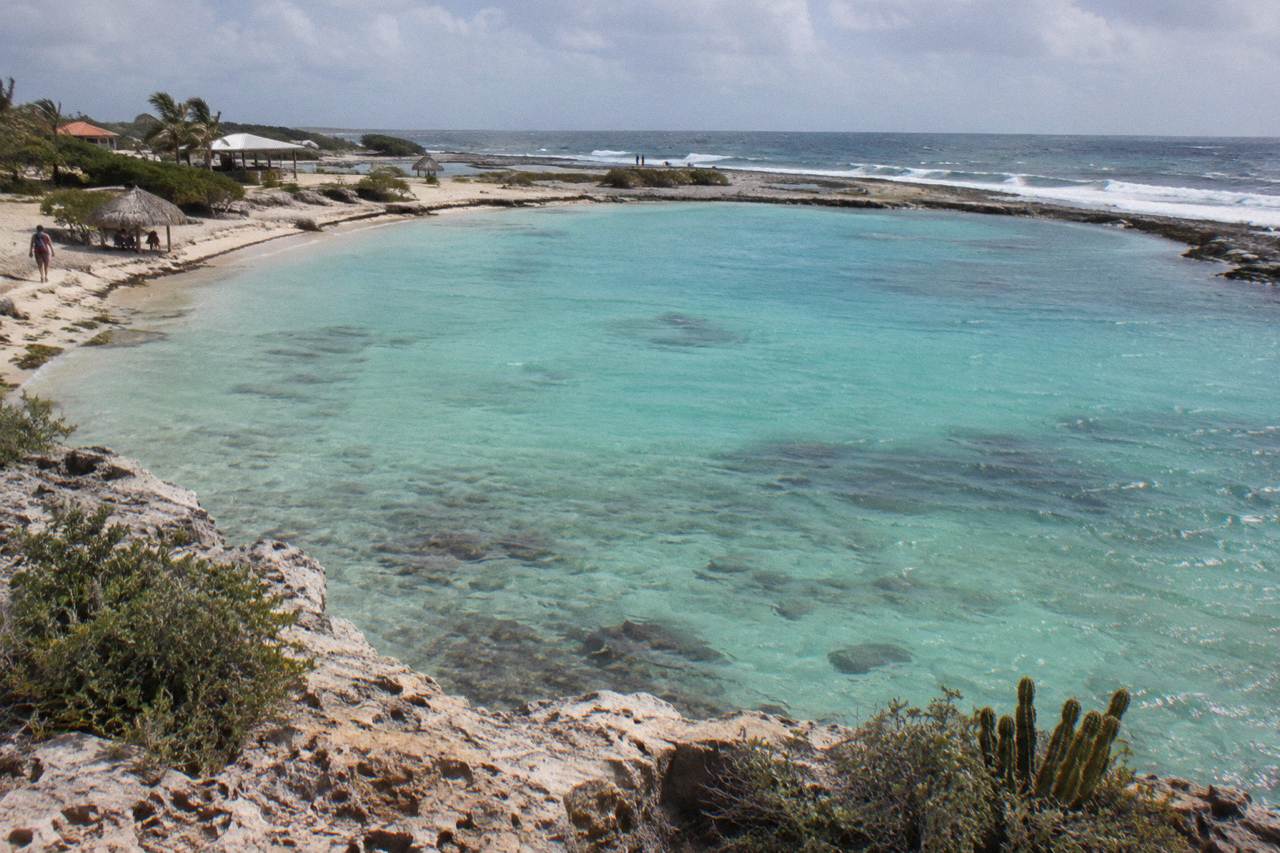 Calm turquoise water over a shallow reef near a wooden pier on Aruba's west coast