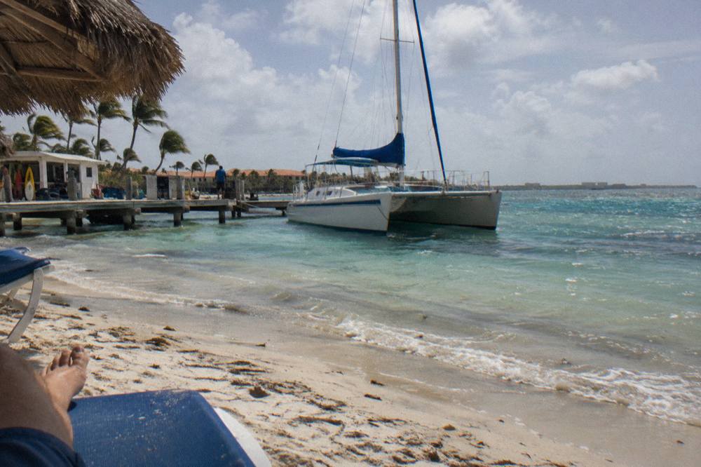 A catamaran moored in calm shallow water near a Palm Beach pier