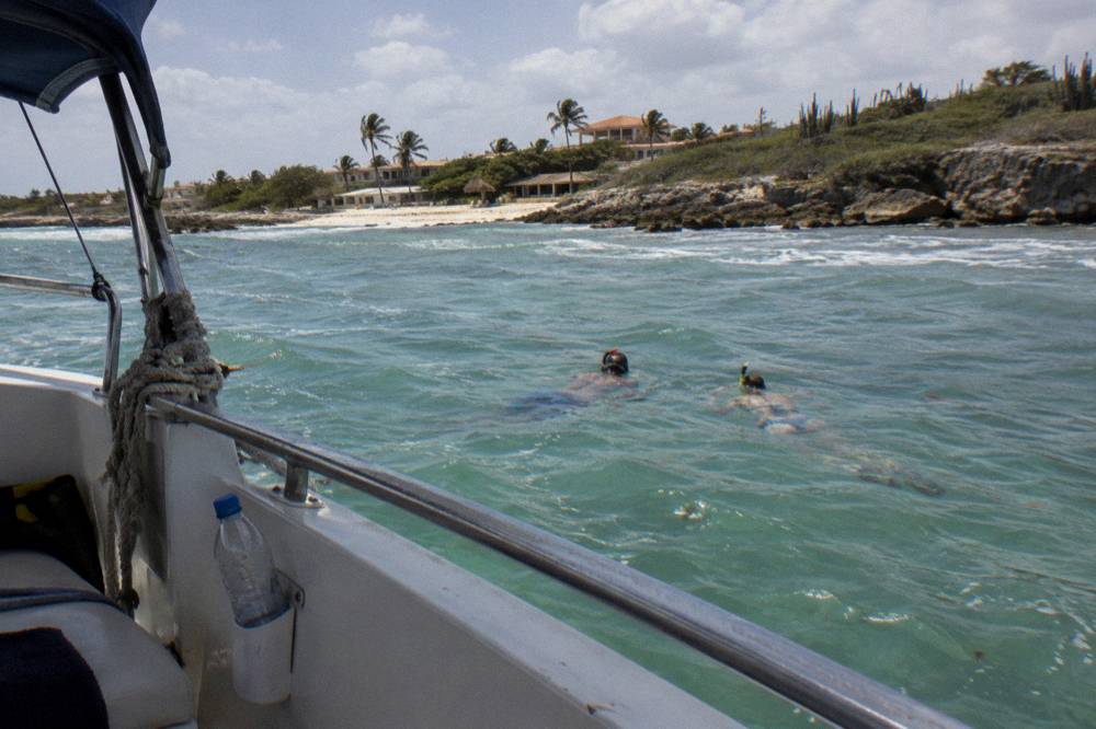 Snorkelers resting on a shaded bench at the front of a boat in calm water