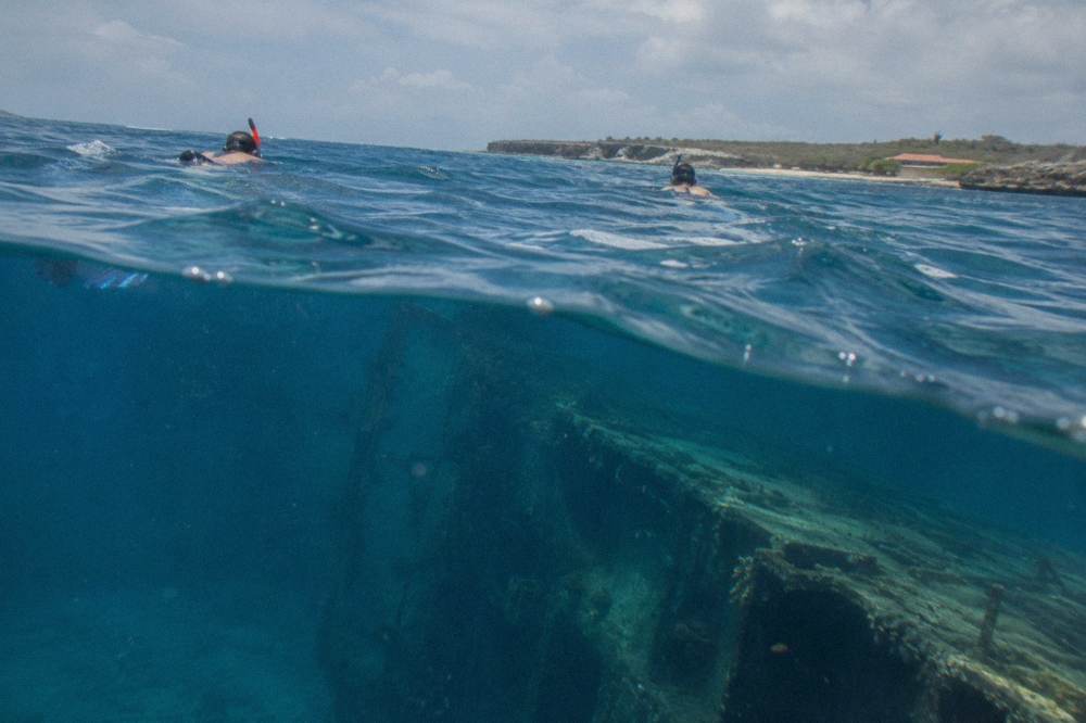 Snorkelers in deep blue water above the shadow of a large sunken ship hull