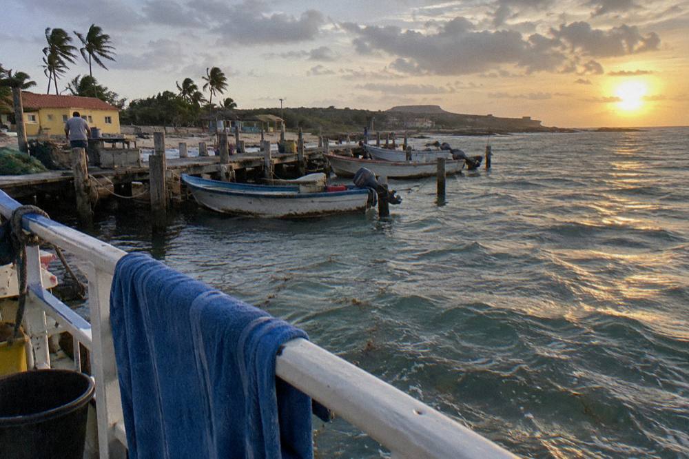 Sun sinking into the sea past a quiet boat railing